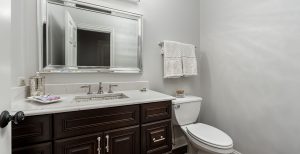 Bathroom vanity with white countertops and dark cabinets next to a toilet