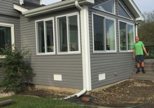 Happy homeowner standing next to home addition with gray siding