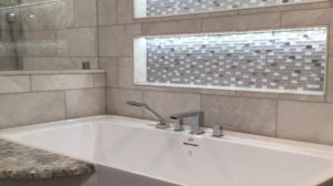 Close up of modern bathtub with silver fixtures and gray backsplash